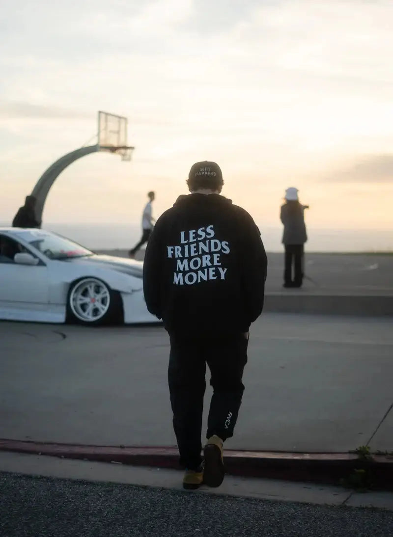 Person wearing black hoodie with 'Less Friends More Money' print