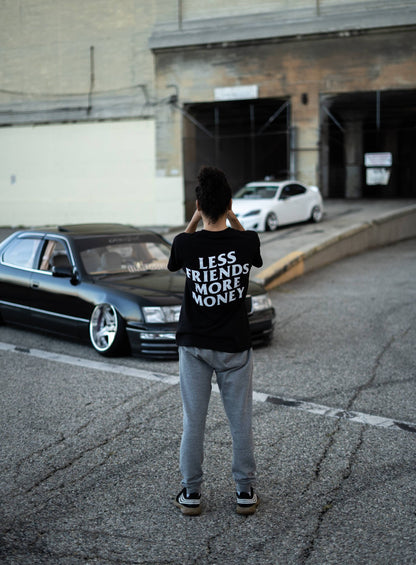 Person wearing black tee with 'Less Friends More Money' print